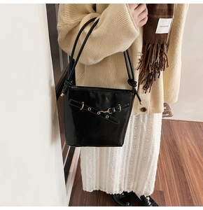 Détail du sac seau élégant en cuir verni noir avec boucle en métal et bandoulière fine