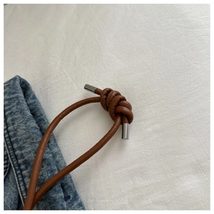 Close-up of brown leather drawstring with silver metal tips and knot detail on casual bag