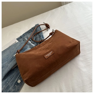 Detail of brown matte leather bag with embossed logo and knotted rope strap in cozy setting