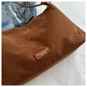 Close-up of brown frosted shoulder bag with leather logo patch and zip closure