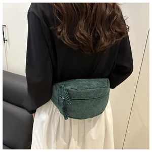 Detail showing deep green corduroy waist bag texture and woven zipper pull on model