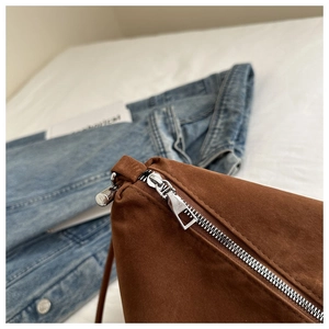 Detailed close-up of silver metal zipper and soft brown suede texture on a crossbody bag