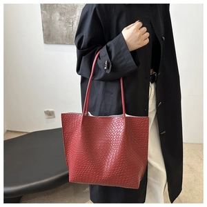 Detail of red snake-patterned tote bag held by a model in a minimalist setting
