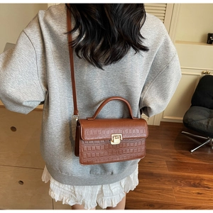 Detail of a brown crocodile pattern handbag with gold metal lock worn by a model