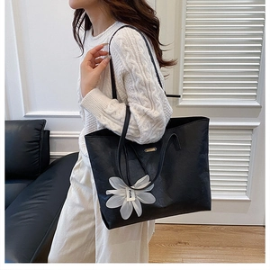 Macro detail of a large black leather tote bag featuring a white floral charm accessory