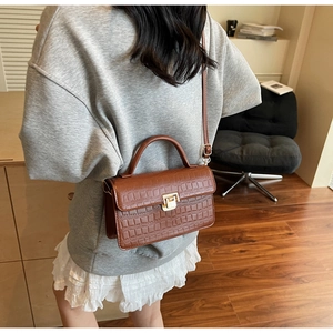 Detail of a brown faux leather crossbody bag with crocodile pattern and golden metal lock