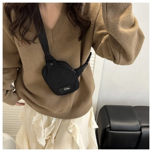 Close-up of a black mini chest bag with adjustable strap worn by a model in a cozy room