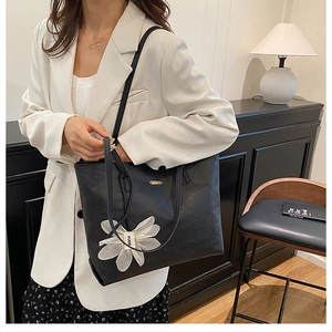 Close-up of a large black tote bag with gold logo and white flower pendant detail