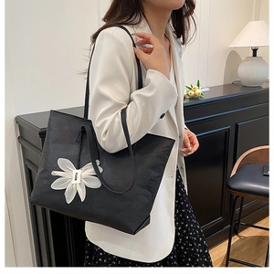 Detail einer großen schwarzen Totebag mit Ledertextur und weißem Blumenanhänger