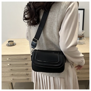Detail of minimalist black crossbody bag with decorative triple stitching and gold buckles