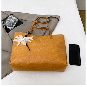 Close-up of pleated yellow tote bag with white silk flower charm on textured leather