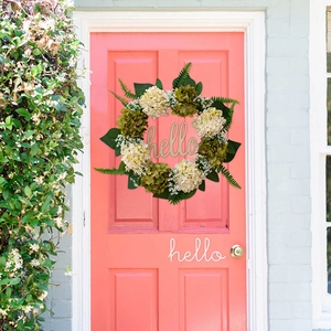 Close-up of decorative hydrangea wreath with hello sign hanging on a pink front door