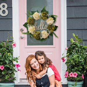 Detail of a white hydrangea door wreath with greenery and a golden hello sign
