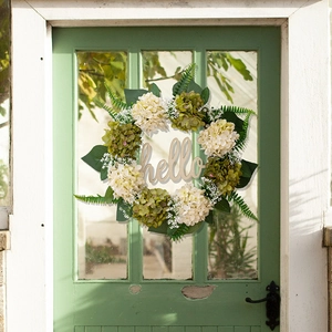 Detail of faux hydrangea wreath with green leaves and a wooden hello sign on a door