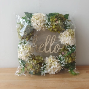 Detail of faux hydrangea wreath with green leaves and a hello wooden sign in packaging