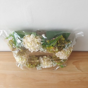 Detailed view of white hydrangea wreath with green leaves in protective plastic bag