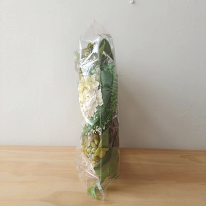 Detail of faux white hydrangea wreath with green leaves in protective packaging