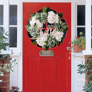 Detail of faux hydrangea wreath with wooden hello sign on a vibrant red front door