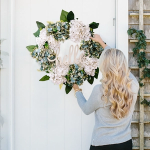 Detail of faux hydrangea wreath with wooden hello sign hanging on a white front door
