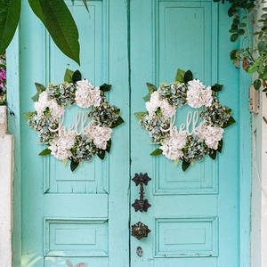 Close-up of artificial hydrangea wreaths with wood hello sign on a blue door