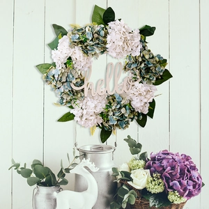 Detail of faux hydrangea wreath with green leaves and a wooden hello sign on white door
