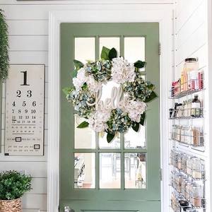 Detail of faux hydrangea wreath with hello sign on a green front door setting