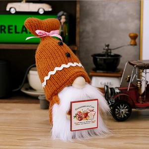 Close-up of knitted orange gnome holding a wooden Gingerbread Cafe sign ornament
