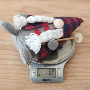 Christmas gnome doll with red and blue plaid hat being weighed on a scale at 138.7 grams