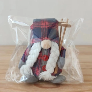 Detail of Christmas gnome plush with red plaid hat, white braids, and wooden ski poles