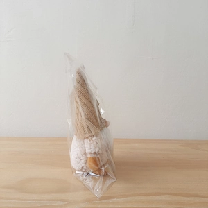 Detail view of a knitted Christmas gnome plush with beige hat and white beard in packaging