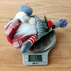 Nordic Christmas gnome plush with grey knitted hat being weighed on a silver digital scale