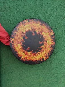 Detail of a black percussion drum with orange flame pattern held on a green surface