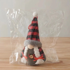 Detail of a Christmas gnome with red and black plaid hat and white braids in clear packaging