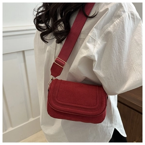 Detail of red suede crossbody bag with wide shoulder strap shown on a model