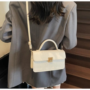 Detailed view of white crocodile pattern handbag with gold hardware on a model