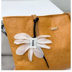 Detail of yellow pleated leather tote with white floral charm and golden brand plaque