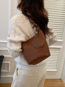 Borsa a secchiello marrone scuro con tracolla intrecciata e texture scamosciata sul modello