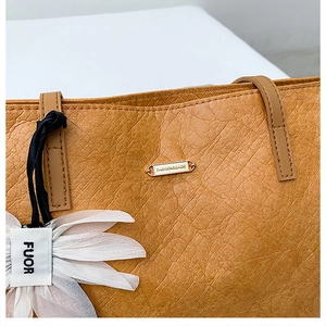 Close-up of brown crinkle leather tote bag with gold metal plaque and daisy charm detail