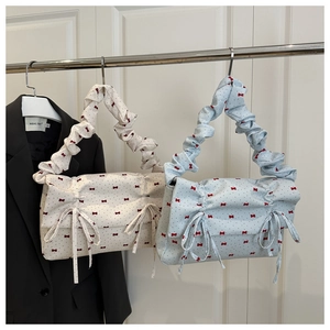 Detail of pleated cloud shoulder bags with red bow patterns in beige and light blue