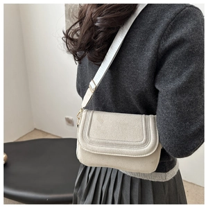 Detail of beige crossbody bag with U-shaped stitching and grey nylon strap on model