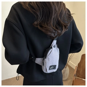 Detail view of a light gray mini chest bag with adjustable black strap on a model