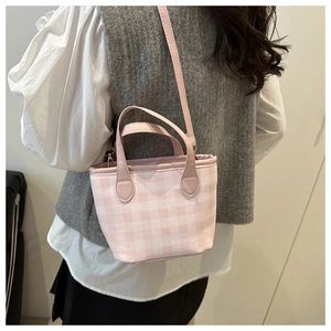 Pink and white checkered canvas bucket bag with adjustable leather strap worn by a model