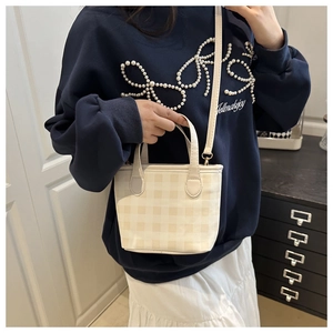 Close-up of a cream plaid handbag styled with a long strap and metal hardware details