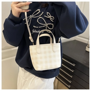Detail of a cream checkered mini tote bag with adjustable strap worn by a model