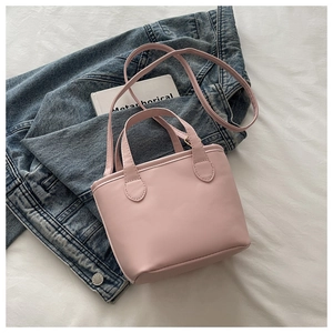 Close-up of light pink PU leather handbag with dual handles and adjustable strap on denim
