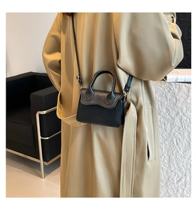 Detailed view of mini black lychee leather handbag with curved handle and slim strap