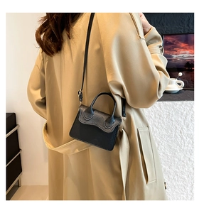 Vue arrière d'un mini sac en cuir noir porté avec un trench-coat kaki en intérieur chic