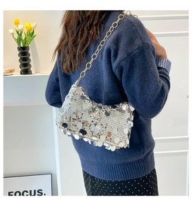 Detail of silver sequin crossbody bag with gold chain strap shown on a model