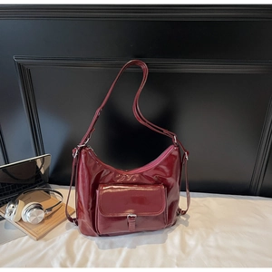 Detail of burgundy glossy leather hobo bag with front metal buckle pocket and zipper