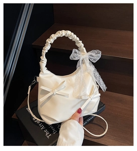 Detail of cream pleated handle and lace bow decoration on a soft leather cloud bag